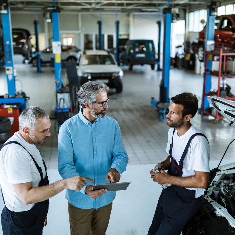 Mid adult manager using digital tablet while talking to mechanics in auto repair shop.