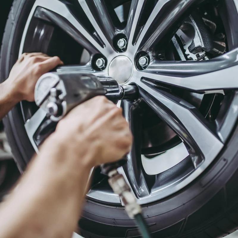 Cropped image of handsome mechanic is working in auto service. Car repair and maintenance. Twisting/untwisting bolts on wheel.