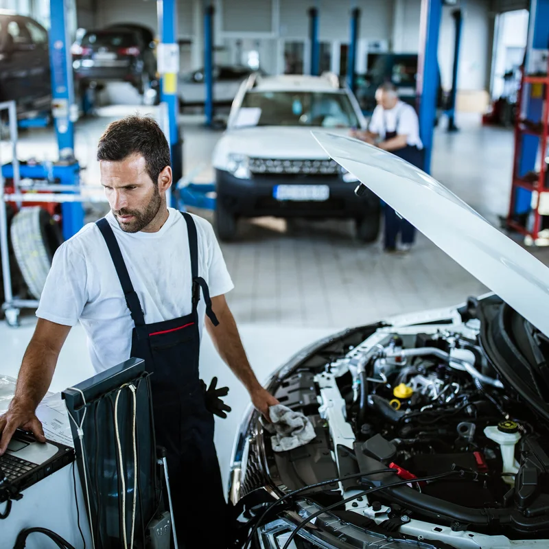 Young mechanic using computer while working on car diagnostics in a repair shop.